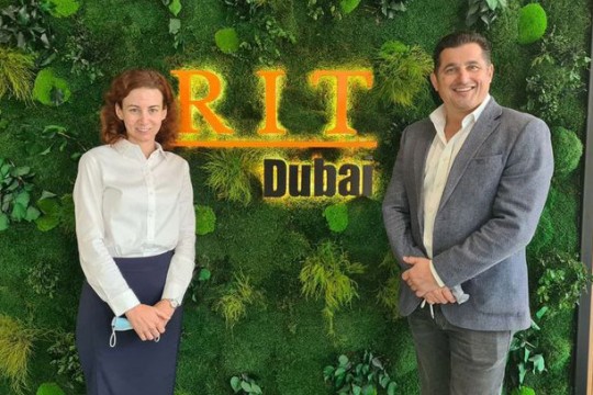 two people standing in front of a wall of plants around a sign for RIT Dubai.