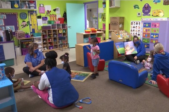 children and workers at a day care facilities sitting on the floor and playing.