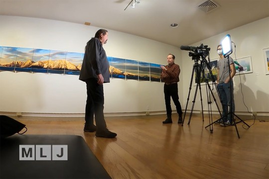man being interviewed in front of a camera in an art studio.