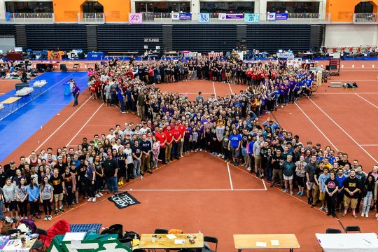 hundreds of people gathered in the shape of a ribbon.
