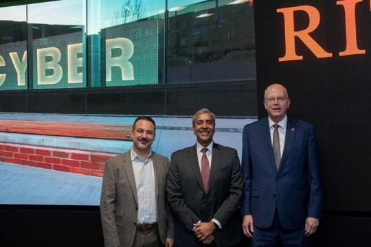 three men standing in front of a video screen.