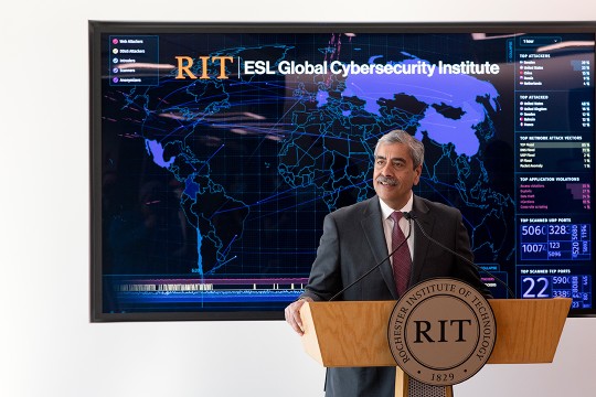 man speaking at a podium with a large map of the world behind him.