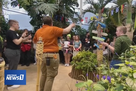 museum patrons listening to a staff member and a sign language interpreter in a butterfly garden.