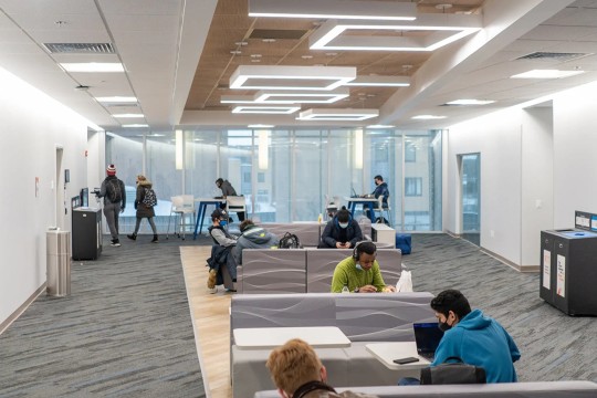 a lounge with students sitting, eating, walking and working.