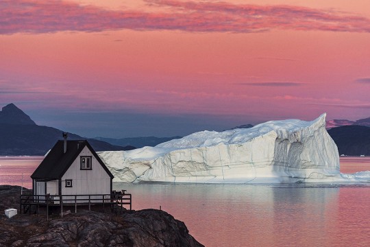 scene of a small house and an iceberg in Greenland.