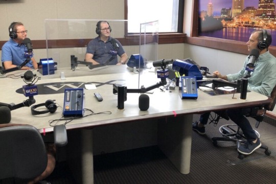 three people with headsets talking into microphones in a radio station.