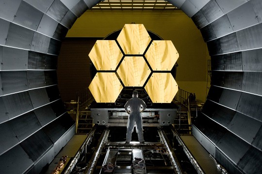 person standing in front of six hexagonal mirrors of the James Webb Space Telescope.