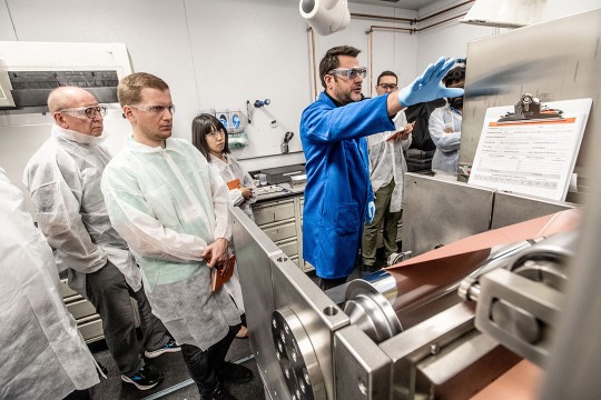 people wearing clean suits watching a demonstration of machinery.
