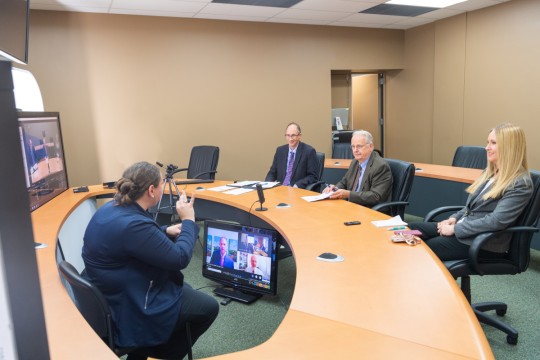 Image of NTID representatives at a table watching a large screen with EPA representatives. An interpreter sits between. 