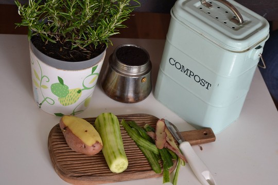 a peeled potato and cucumber on a cutting board next to a tabletop compost bin.
