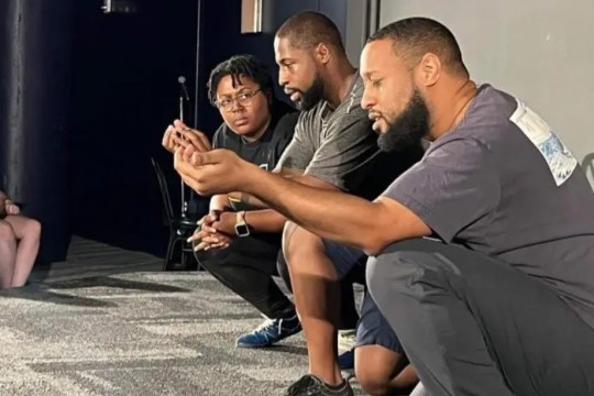 three people in an improv group crouching on a stage.