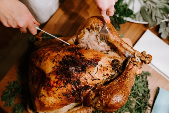 person cutting into a roasted turkey.