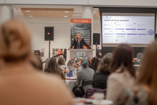 tables of people seated and facing a speaker at a podium.