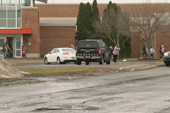 people, cars, and police car outside of a brick building.