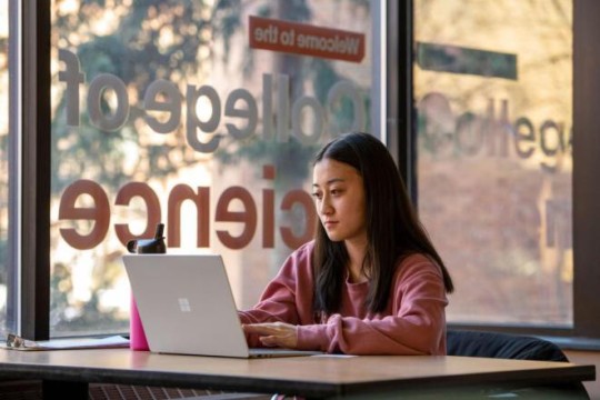 college student sitting at a table working on a laptop.
