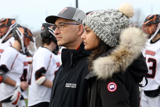 two people watching a lacrosse game from the sidelines.