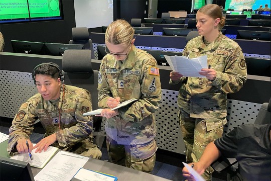 three R O T C cadets wearing military fatigues in a cyber security center.