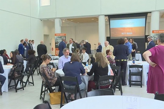crowd of people seated at round banquet tables.