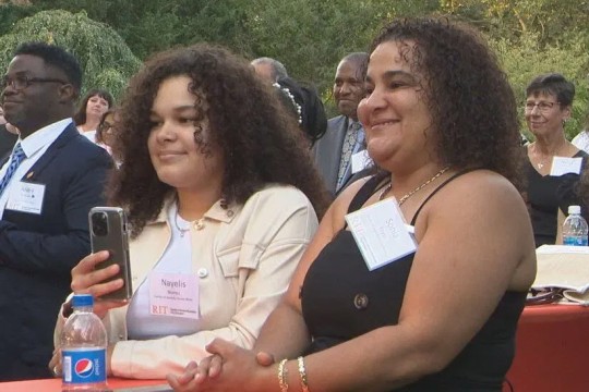 two women standing at a high top table outside.