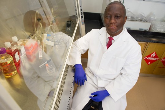 researcher wearing a white lab coat posing in a lab.