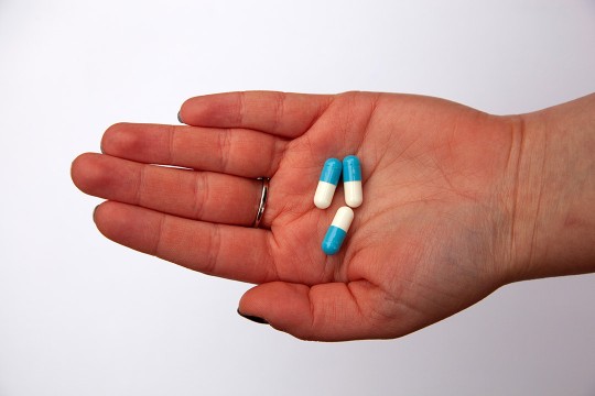 open hand holding three blue and white capsules.