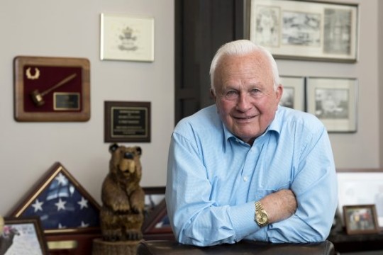 businessman leaning against a desk with his arms folded. 