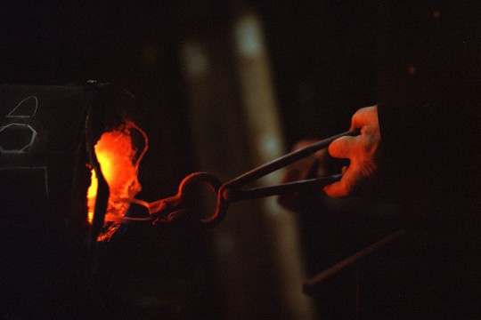 A piece of metal, held with tongs, is heated in a forge.