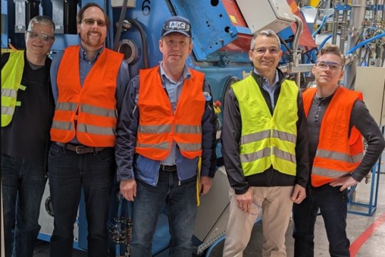 five men wearing high visibility vests standing in front of large industrial equipment.