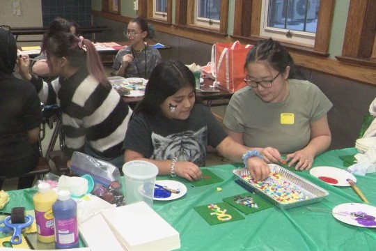college students and elementary school students working at tables on craft projects.