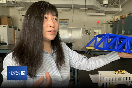 Amanda Bao is shown holding a model of a bridge to explain structural support.