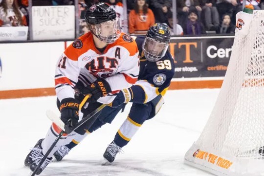 Conor Wilkie is shown playing for the RIT Tigers on the ice coming around the back of the net.