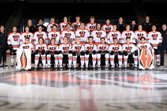 the RIT mens hockey team is pictured with their coaches on the ice in their white game jerseys.