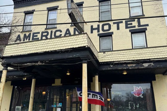 The front facade of the American Hotel is shown with light yellow bricks and black windows.