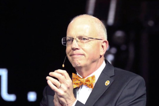 David Munson is shown in a closeup shot standing on a stage clapping.