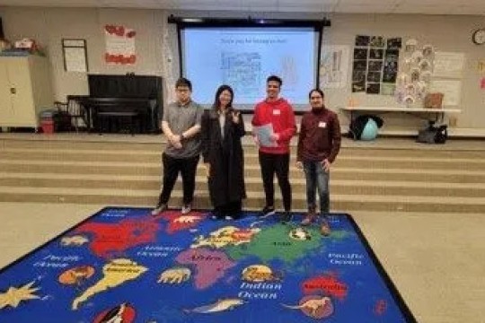 Four English Language program students stand on a rug showing a map of the world in a classroom at The Harley School