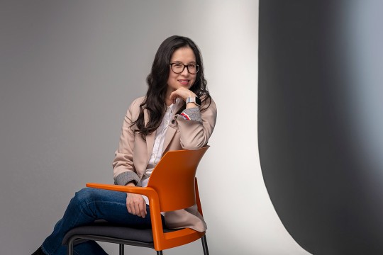 Hye-Jin Nae is shown sitting in an orange chair with her hand posed under her chin.