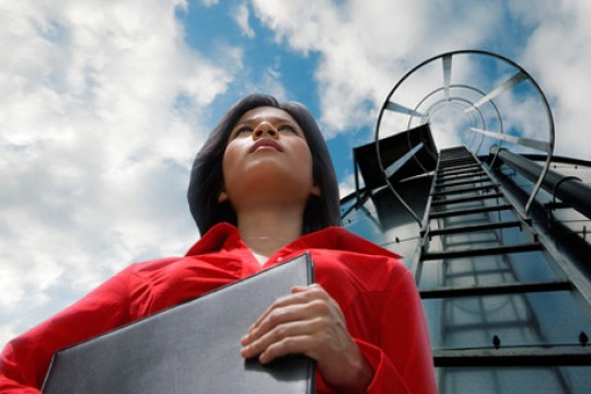 'a woman in a red shirt holds a laptop and stands in front of a silo.'