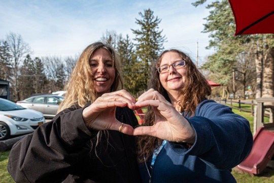 two women are shown making a heart with their hands.
