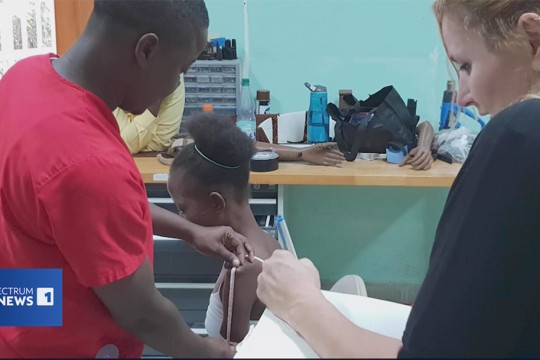 Two adults measure a childs arm for a 3 D printed prosthetic.