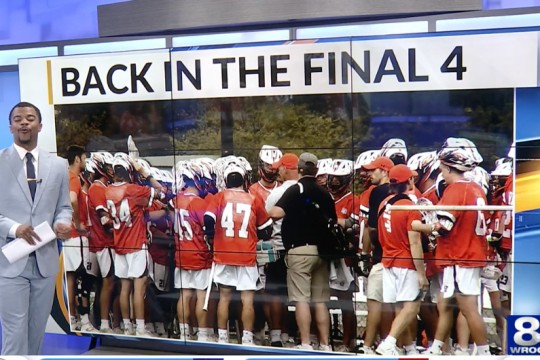 a news anchor stands in front of an image of the R I T mens lacrosse team with the words Back in the Final 4 across the top of the screen.
