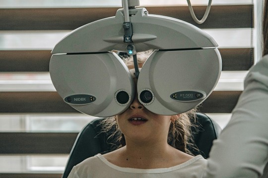 a child sits behind an eye test machine in an eye doctors office.