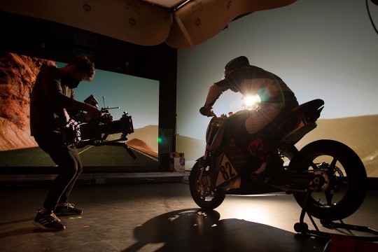 a videographer takes a video of a man on a motorbike in a studio.