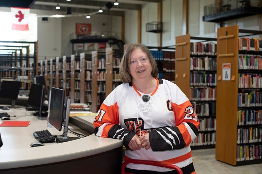 A woman in a celebratory hockey jersey stands at a library front desk.
