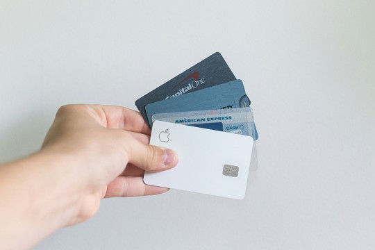 a hand holds four credit cards against a white background.