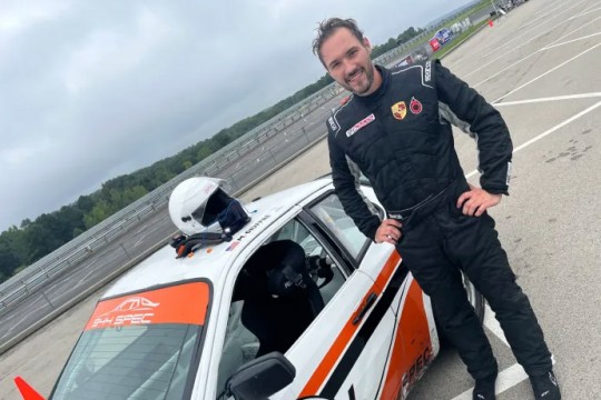a man in a racing suit stands next to a racecar.