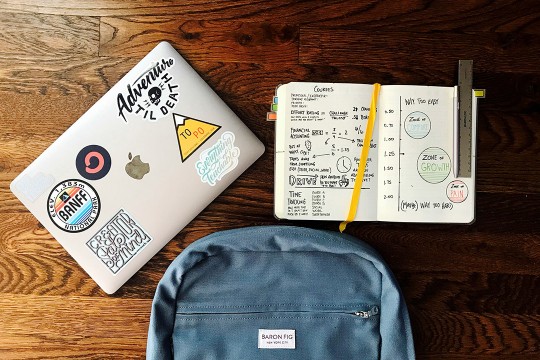a backpack and laptop are shown laying on a table next to an open notebook.