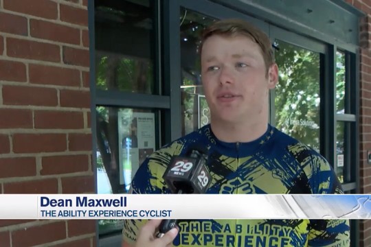 a college age male is shown in biking gear speaking to a journalist.