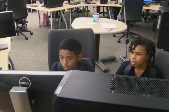 two young children sit next to each other looking at computer screens.