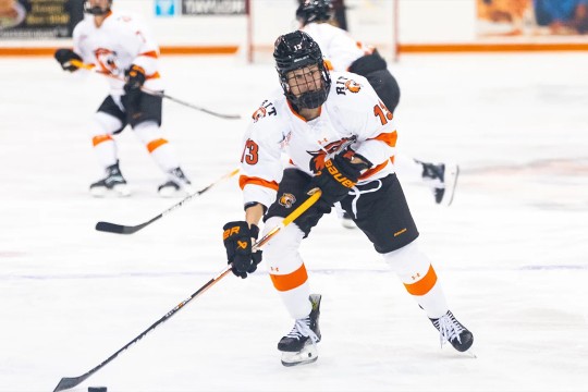 An action shot of Addie Alvarez skating on the ice with a hockey stick in hand, wearing her RIT team uniform.