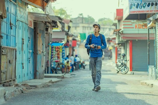 a student of south asian descent walks down a cobblestone street in an appearingly depressed neighborhood